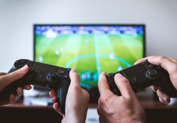 Two hands holding a gaming remote and playing a video game on a TV.